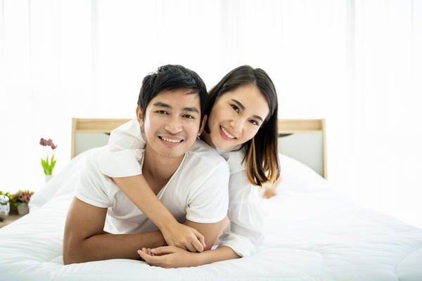 Smiling couple lying together on a bed in a bright bedroom, illustrating family planning and fertility treatment considerations.